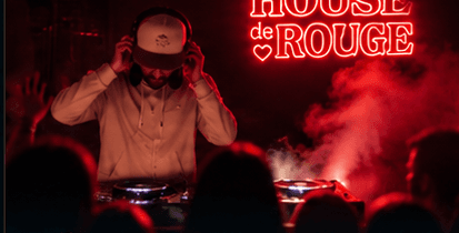 DJ mit Kopfhörern hinter den Decks vor roter Neonschrift, davor die Silhouetten der Gäste