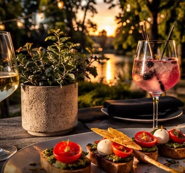 Bruschetta und ein Beeren-Spritz auf dem Tisch an der Terrasse, dahinter der Fluss im Sonnenuntergang