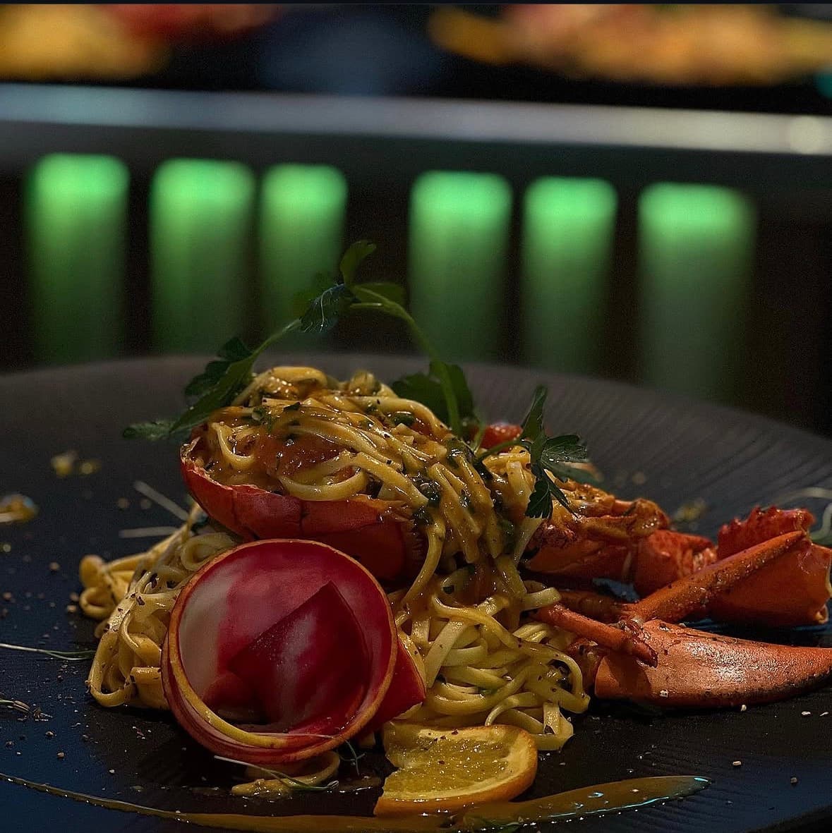 Linguine mit Hummerschwanz und -schere, Radieschenblüte und karamellisierter Zitrone vor der grün beleuchteten Bar