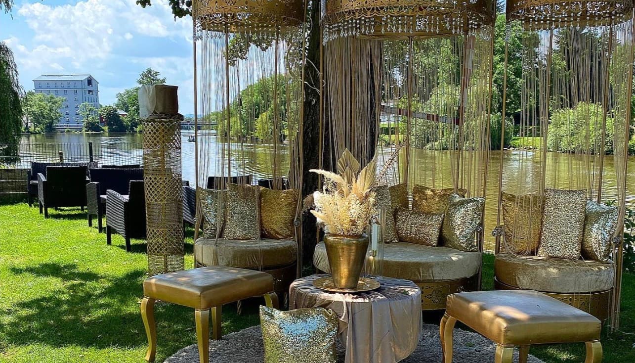 Goldene Lounge-Kabanen unter einem Baum auf der Uferwiese, mit Pampasgras und Pailletten-Kissen
