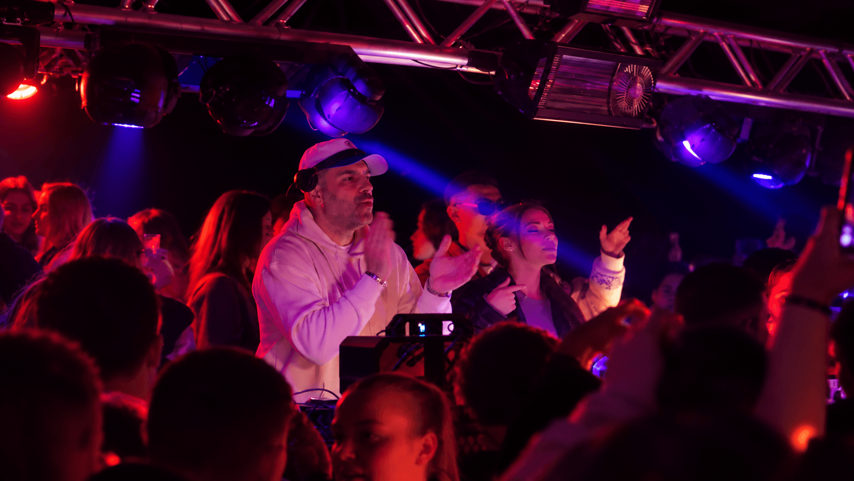 DJ mit weißer Cap klatscht mit der Menge unter blauen Scheinwerfern